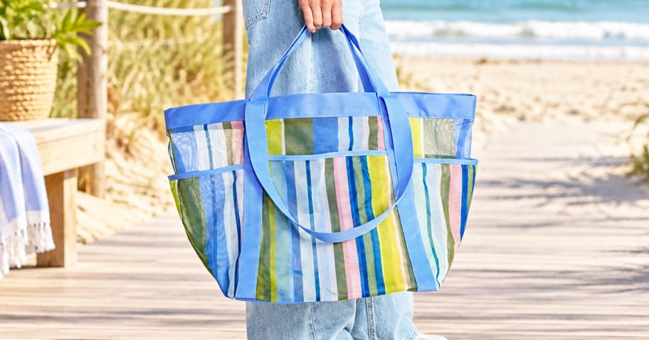 woman holding a blue striped mesh tote bag at beach