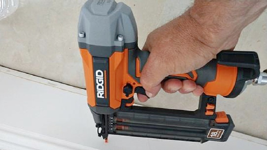 A person's hand holding a RIDGID 18-gauge brad nailer against a white trim molding surface.