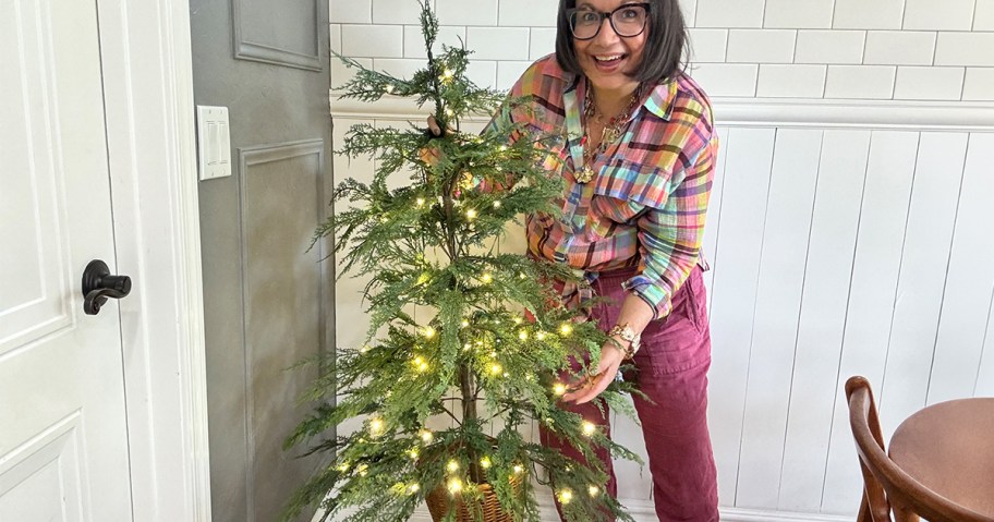 Smiling woman holding a 4 foot cypress Christmas Tree in a dining room