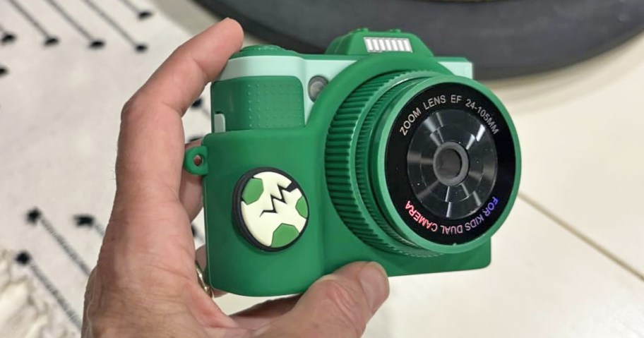 hand holding up a green kids digital camera with dinosaur egg on it