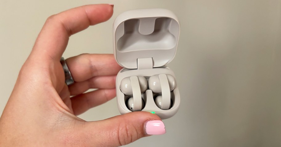 hand holding tan sony earbuds in their charging case