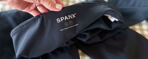 Hand folding back the waist of a pair of Spanx leggings to show the brand