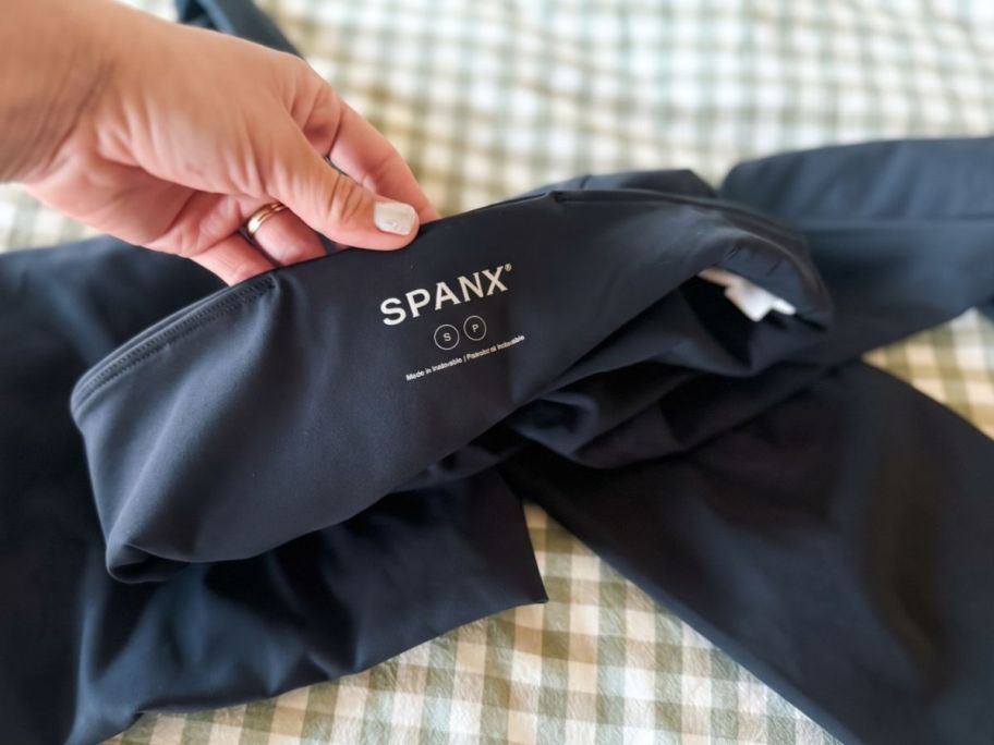 Hand folding back the waist of a pair of Spanx leggings to show the brand 