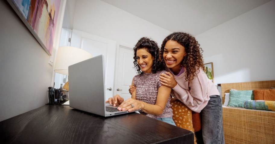woman and young girl looking at a laptop screen sitting on desk in bedroom