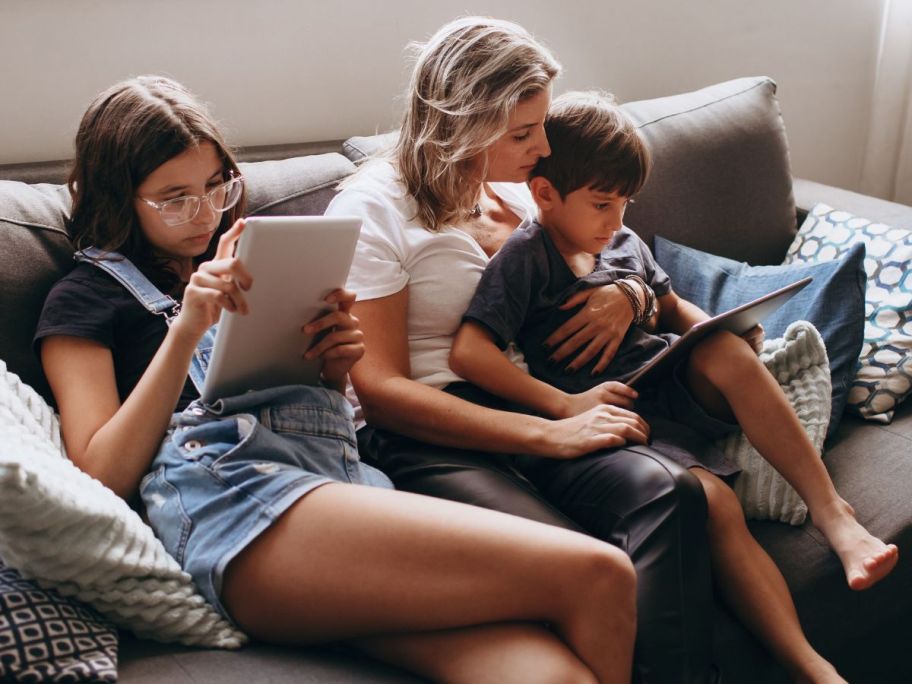 a mom and two kids on a couch using electronic devices