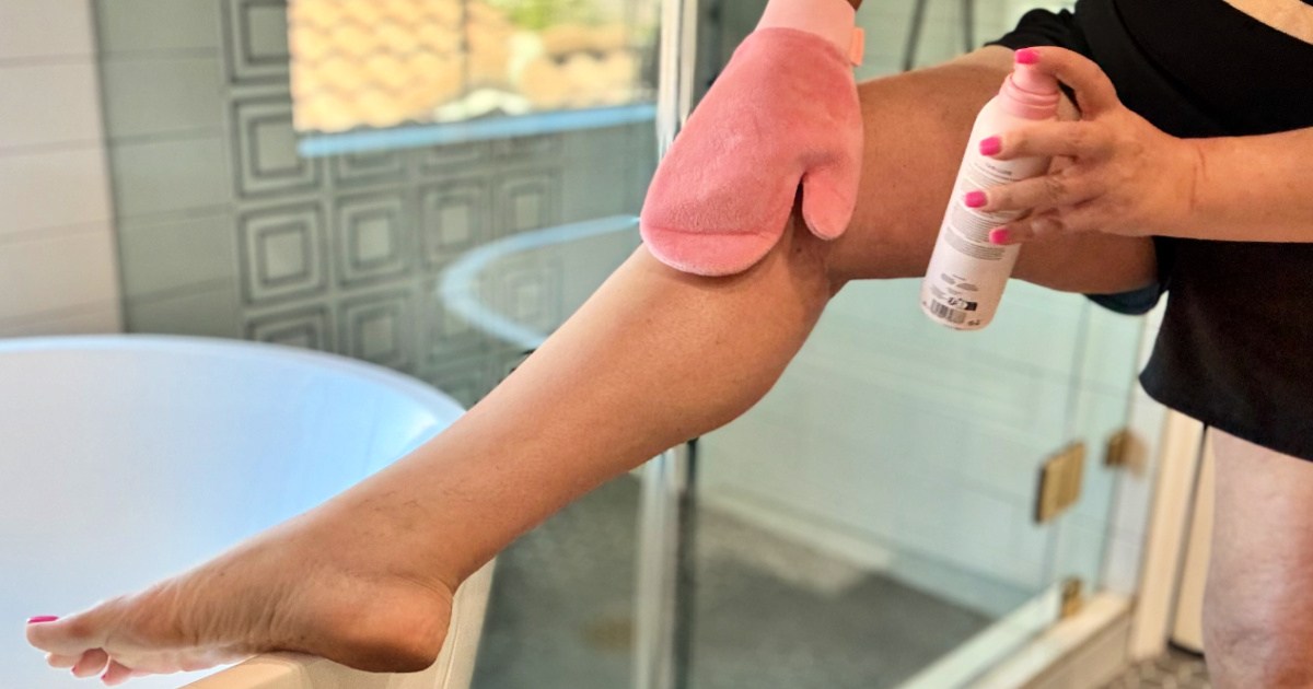 Woman applying tan Luxe spray to leg with pink mitt