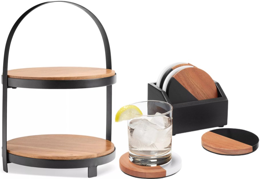 A two-tier wooden tray with a black metal frame and handle, a glass of water with ice and a lemon slice resting on a coaster, and a set of matching coasters in a black holder on a white background.
