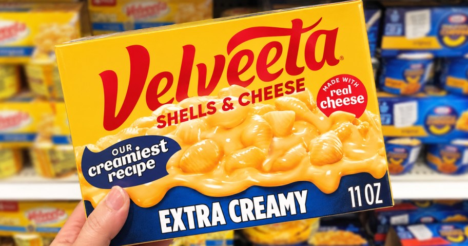 hand holding up a box of Velveeta Extra Creamy Shells & Cheese in store aisle
