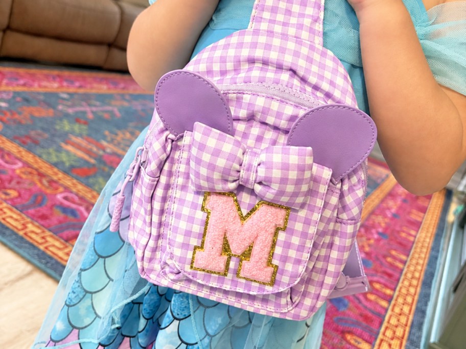 girl in a blue dress with a purple sling bag with mouse ears and letter M initial patch