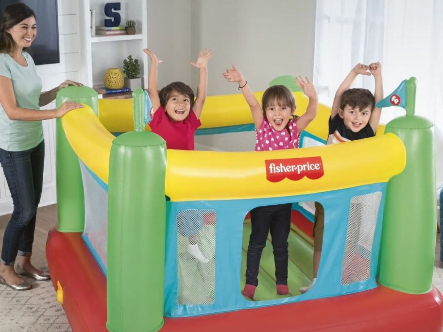 A mom and 3 kids playing with a Fisher Price Bounce House