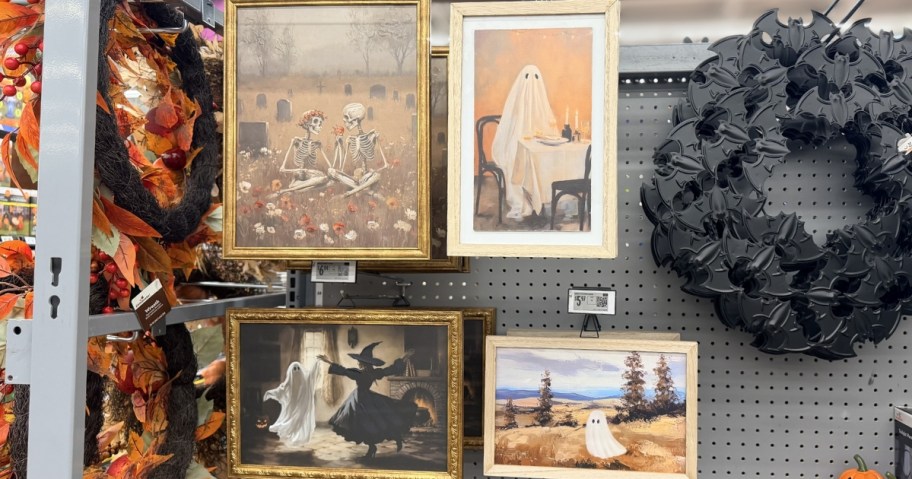 four pieces of halloween framed art hanging in store with black bat wreath next to them