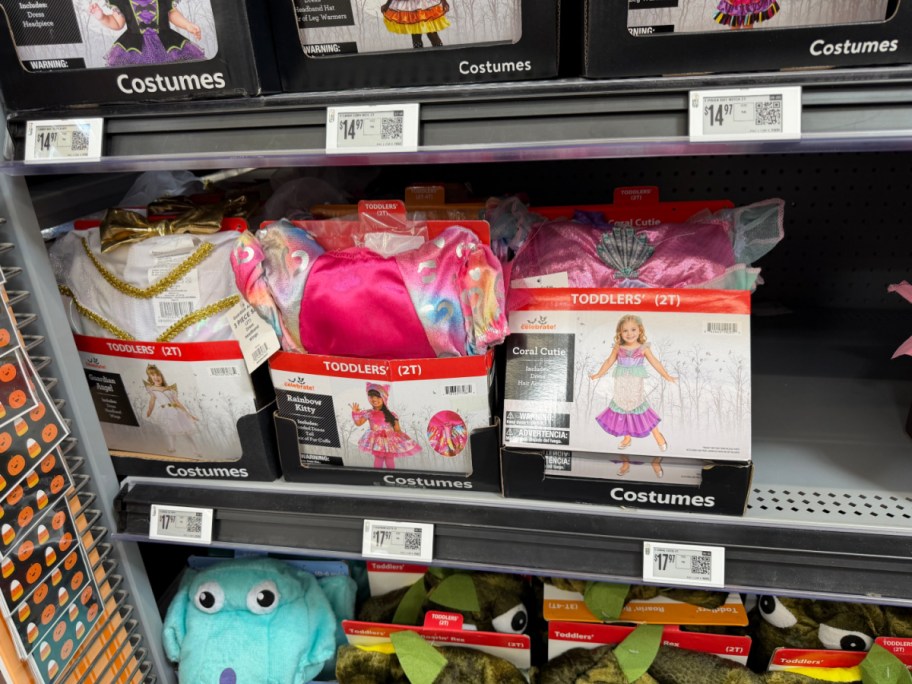 Three Way to Celebrate toddler Halloween costume boxes displayed side by side on a store shelf, featuring a guardian angel costume on the left, a rainbow kitty costume in the middle, and a coral cutie mermaid costume on the right.