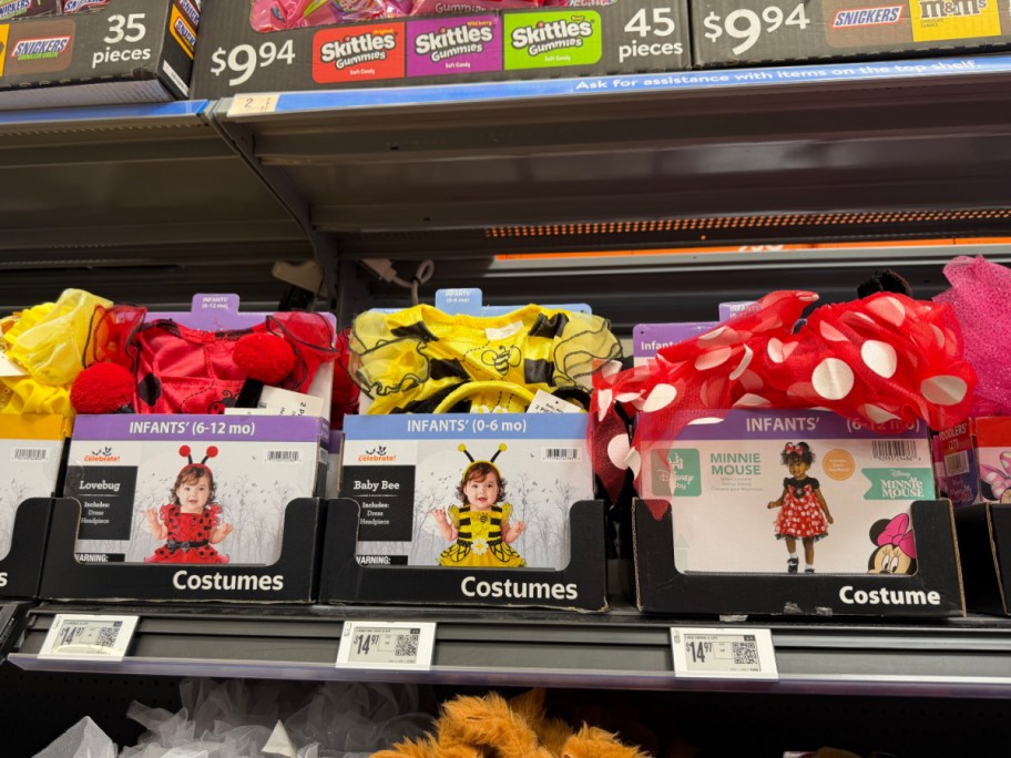 Three Way to Celebrate infant Halloween costume boxes displayed side by side on a store shelf, featuring a Lovebug costume on the left, a Baby Bee costume in the middle, and a Minnie Mouse costume on the right.