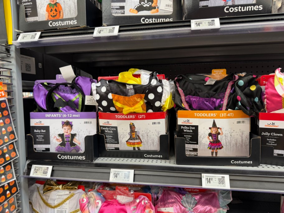 Way to Celebrate Halloween costume boxes displayed side by side on a store shelf, featuring a Baby Bat costume on the left, a Candy Corn Witch costume in the middle, and a Polka Dot Witch costume on the right.