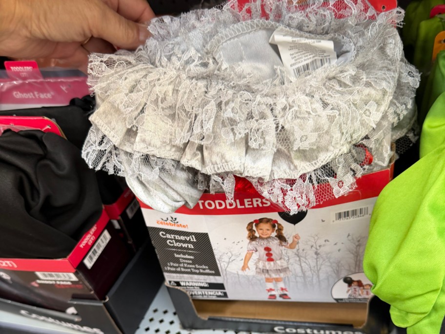 A hand holding a Way to Celebrate toddler Carnevil Clown Halloween costume box with a lace ruff collar on a store shelf.