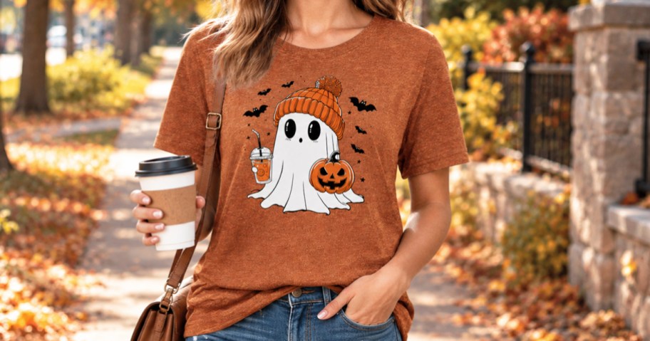 woman wearing a halloween shirt holding a coffee and walking outdoors