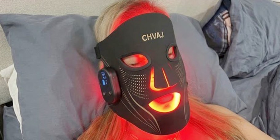 person wearing red light mask in bed