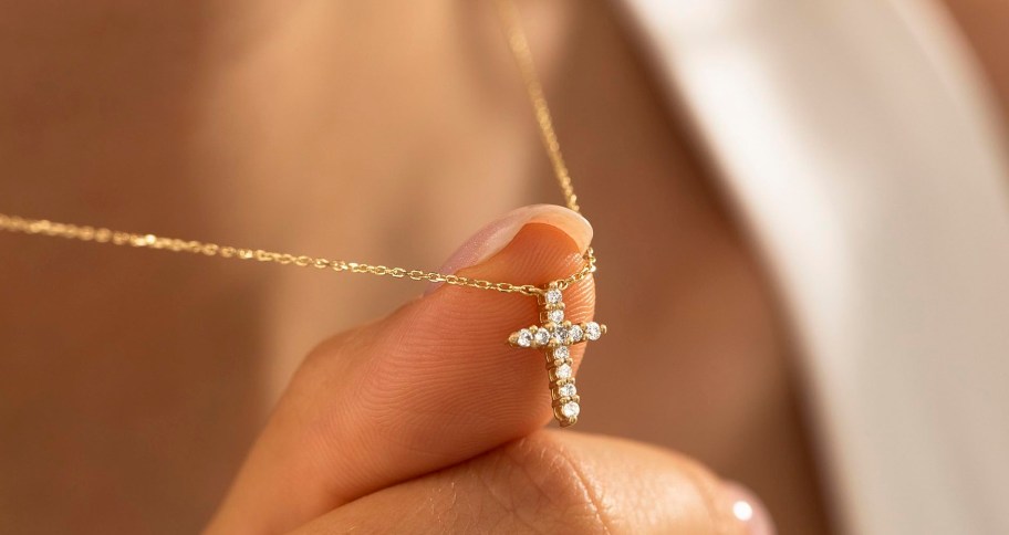 finger holding a diamond cross necklace