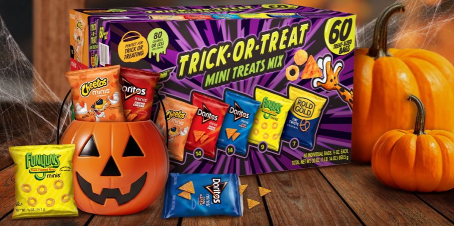 Frito-Lay Trick-or-Treat Mini Treats Mix variety box with 60 snack-sized bags displayed alongside a pumpkin bucket filled with chips, individual snack bags, and pumpkins on a wooden table.