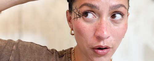 woman with halloween makeup using a wax stick to smooth her spider hairstyle