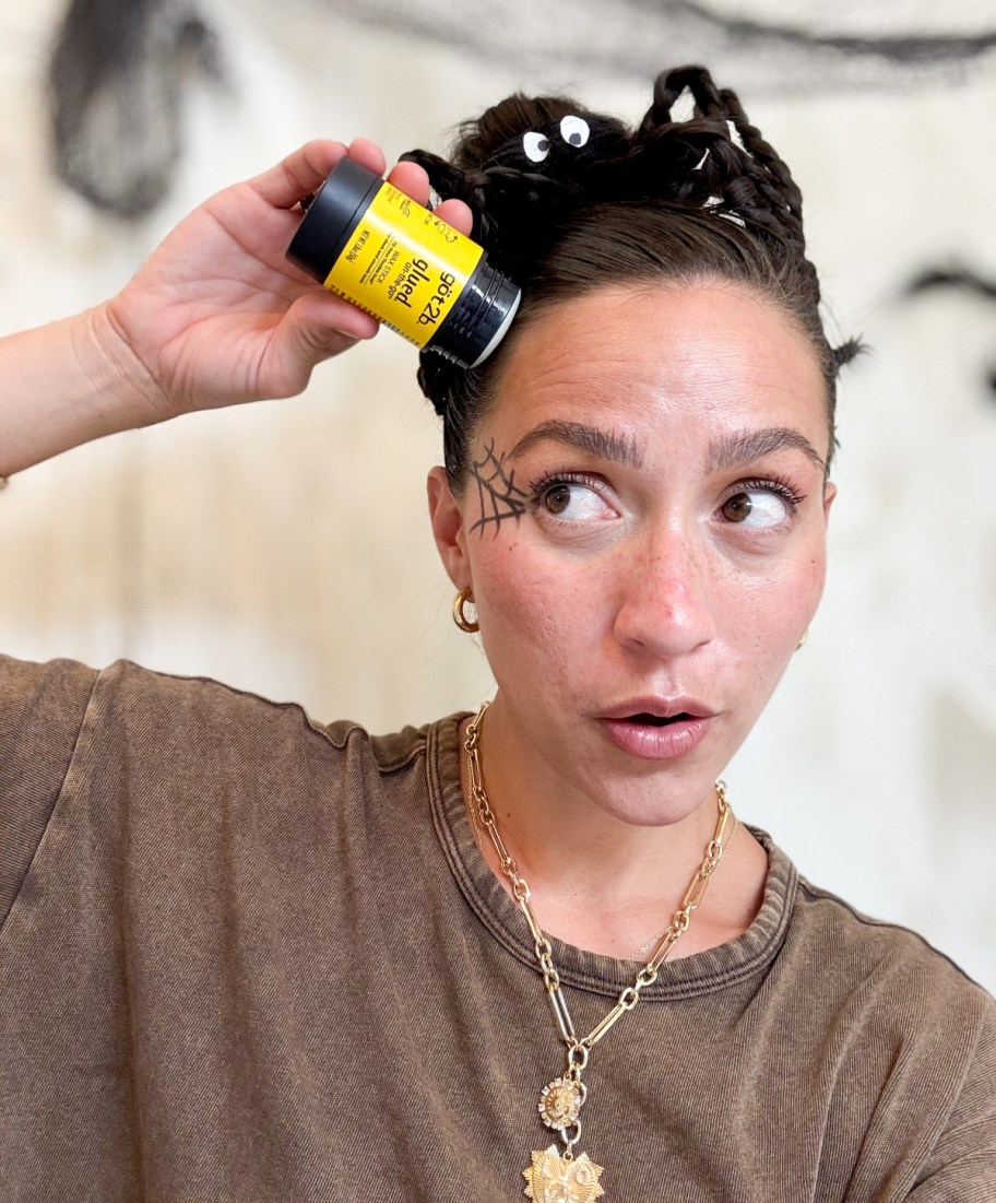 woman with halloween makeup using a wax stick to smooth her spider hairstyle