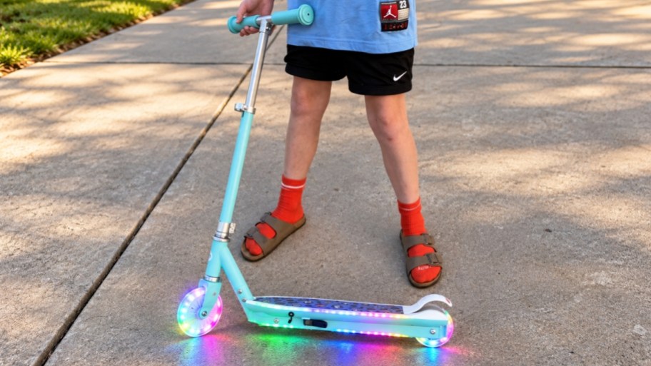 a kid with a light up scooter standing on a sidewalk
