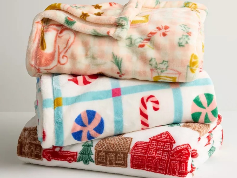 three Christmas themed blankets stacked on top of each other