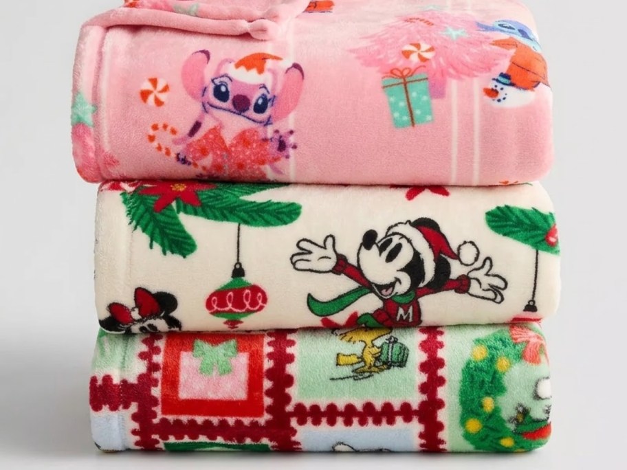 three Disney and Peanuts Christmas throw blankets in a stack