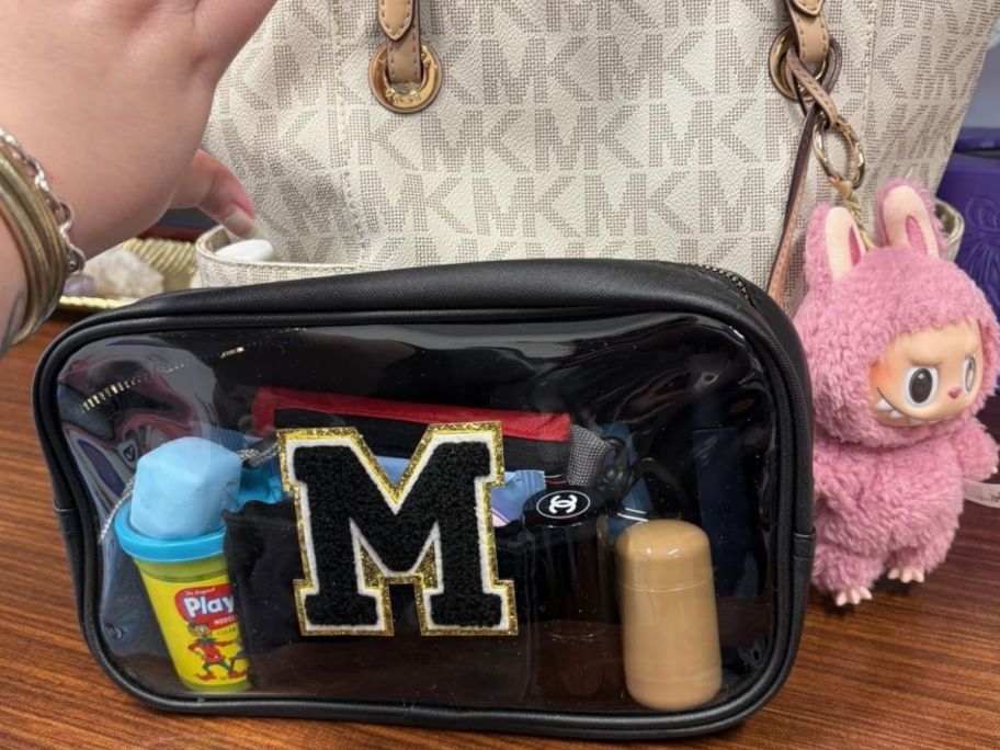 hand holding a makeup bag and a purse with a labubu charm