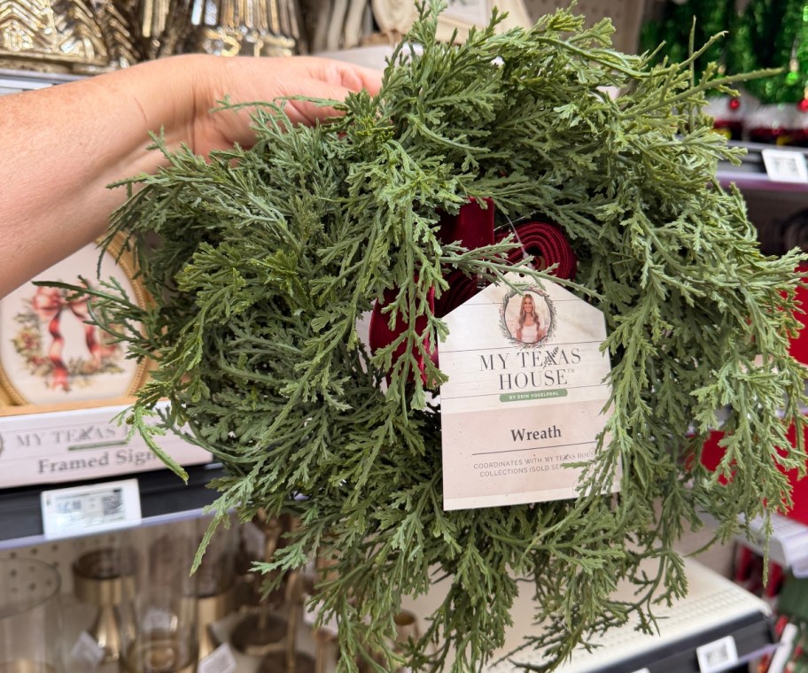 holding a wreath with a red ribbon attached