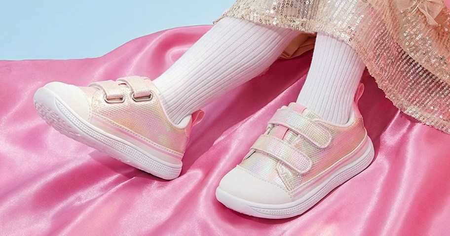 girl wearing a pair of light pink velcro sneakers with a pink satin background