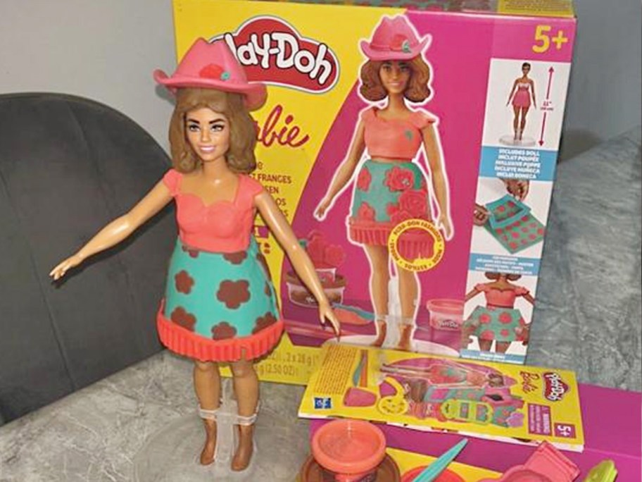 barbie with pink top and hat with box behind it