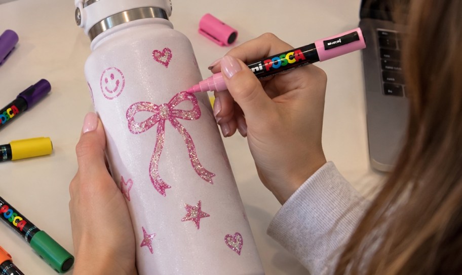 girl drawing on pink water bottle with glitter posca paint marker