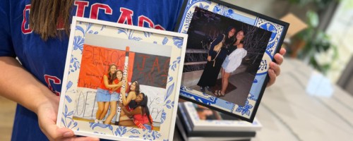 A person holding two custom photo frames with blue and white patterned borders displaying pictures of friends.