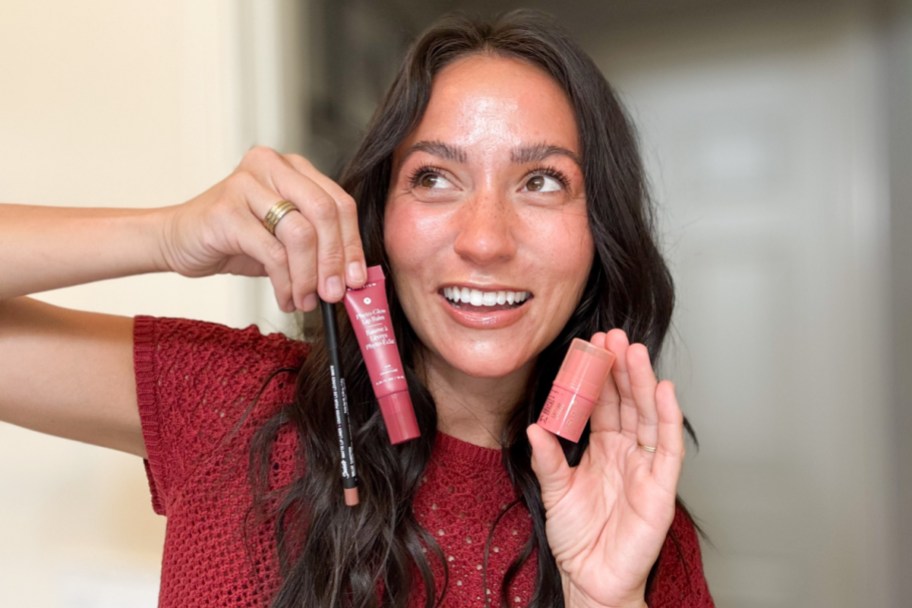 woman holding lip liner, blush stick, and lip balm near face