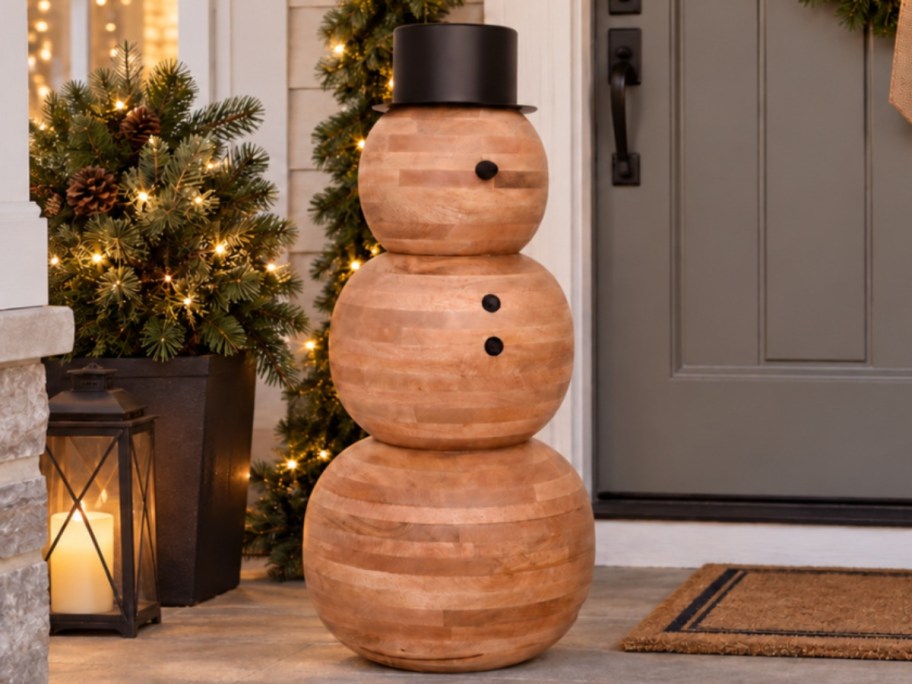 a wooden snowman with a black top hat on a front porch