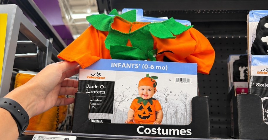 hand reaching for a baby Halloween pumpkin costume on a store shelf