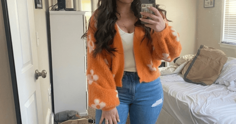 woman in orange cardigan and jeans in a bedroom