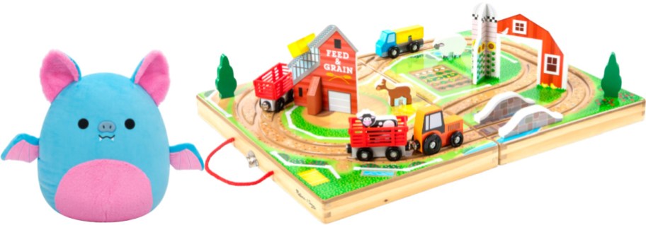 A blue and pink plush bat stuffed animal displayed alongside a wooden fold-out farm train set play case.