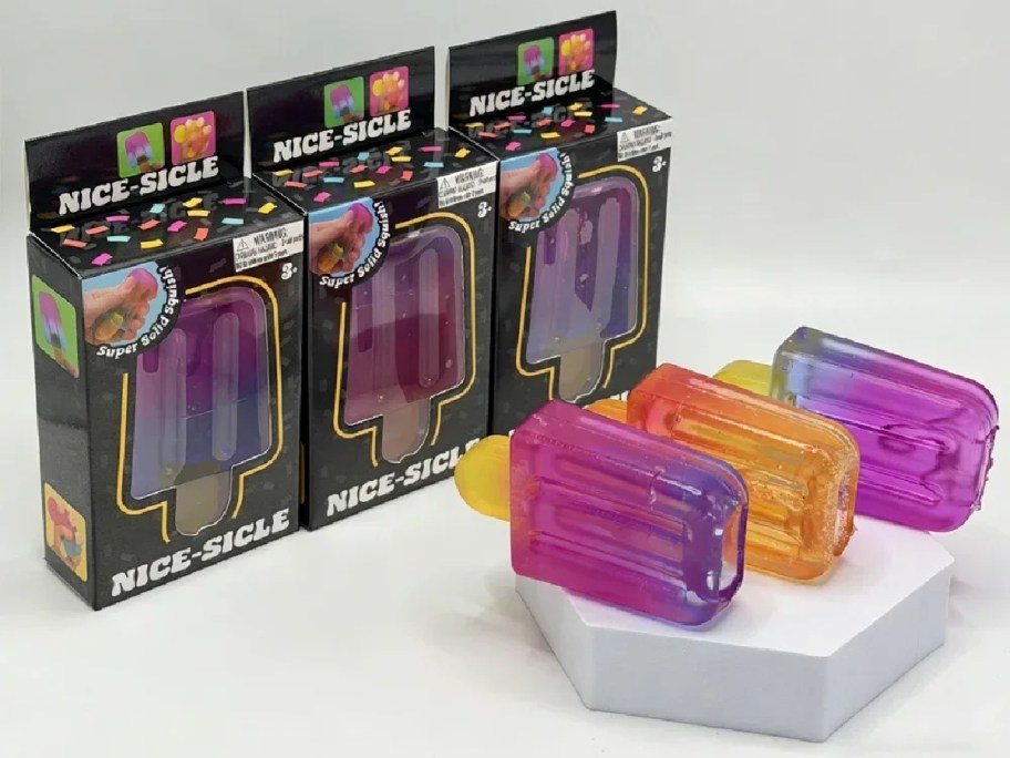 Three Nice-Sicle popsicle blind box packages with three colorful squishy cube popsicles displayed in front of them on a white stand.