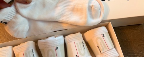 Woman holding up white pair of ankle socks in front of box of five single packs
