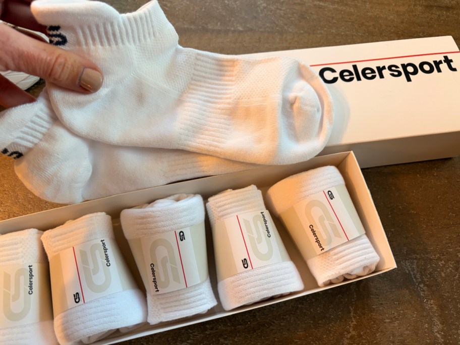Woman holding up white pair of ankle socks in front of box of five single packs