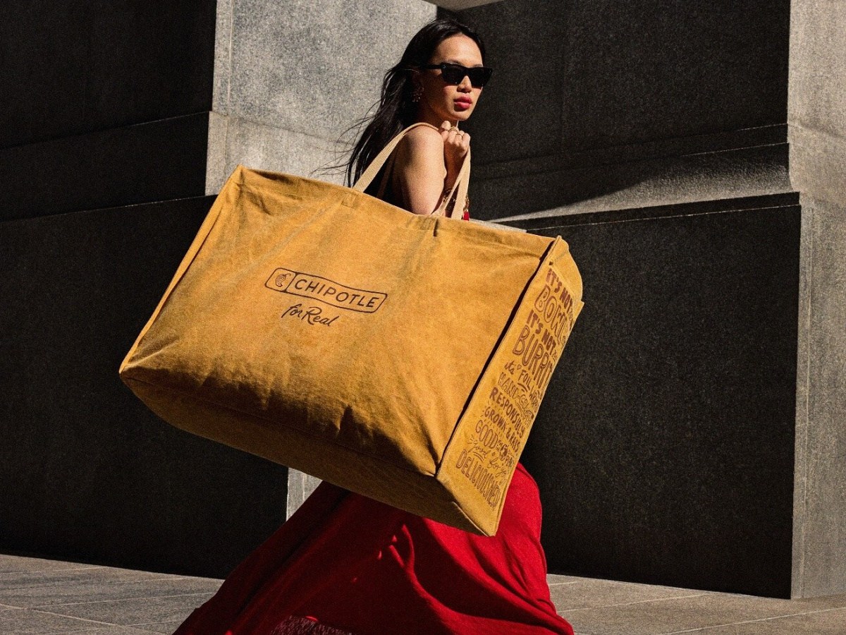 Woman in red dress carrying very large brown Chipotle bag