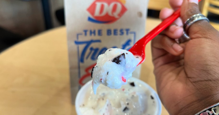 Hand holding up spoonful of dairy queen peppermint blizzard in front of paper bag