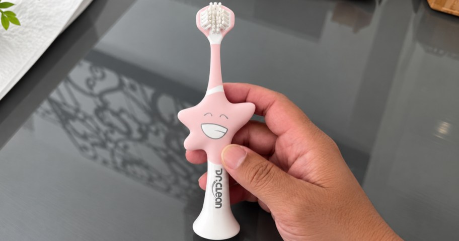 hand holding up a pink star shaped kids toothbrush