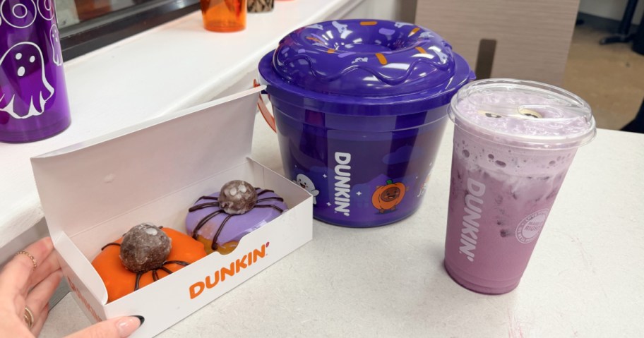 Dunkin spider donuts, munchkin bucket and purple drink on a counter