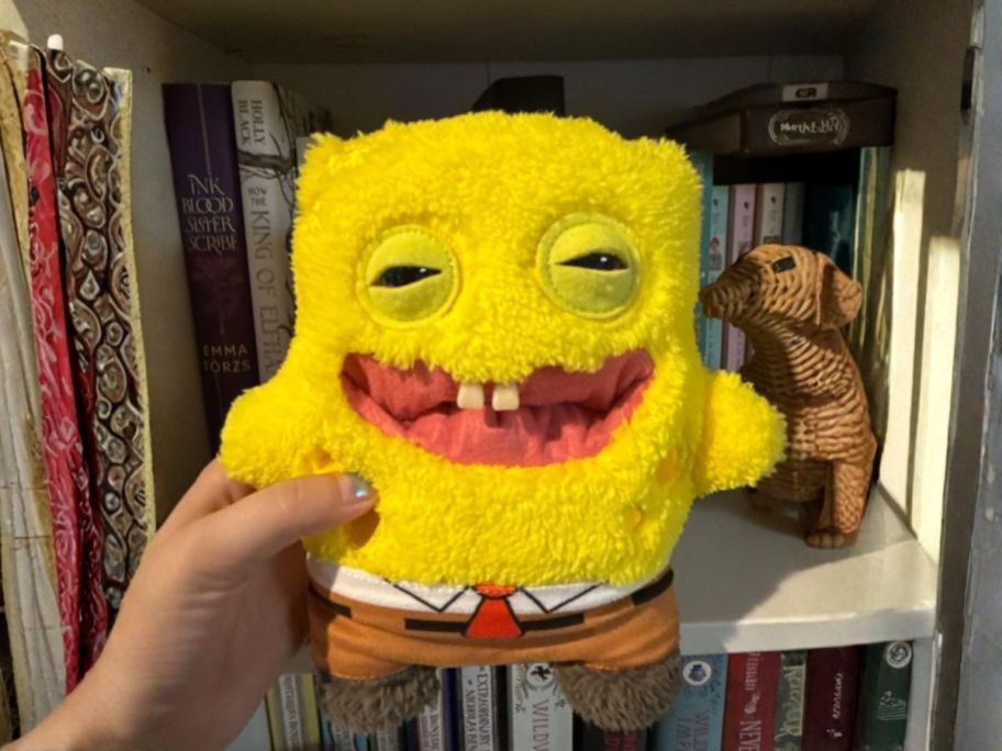 hand holding Fuggler SpongeBob SquarePants 9" Plush in front of books