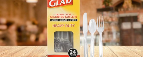 Glad heavy duty crystal clear assorted cutlery 24-pack box with a knife, spoon, and fork displayed upright next to it on a wooden table.