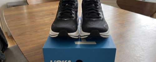 A table with a shoe box with a pair of HOKA Clifton 10 running shoes on it
