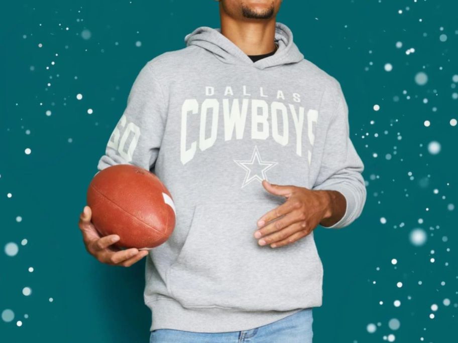 Man wearing a Dallas Cowboys Gray Hoooded NFL Sweatshirt while holding a football